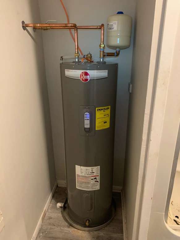 A gray water heater with expansion tank sitting in a closet.