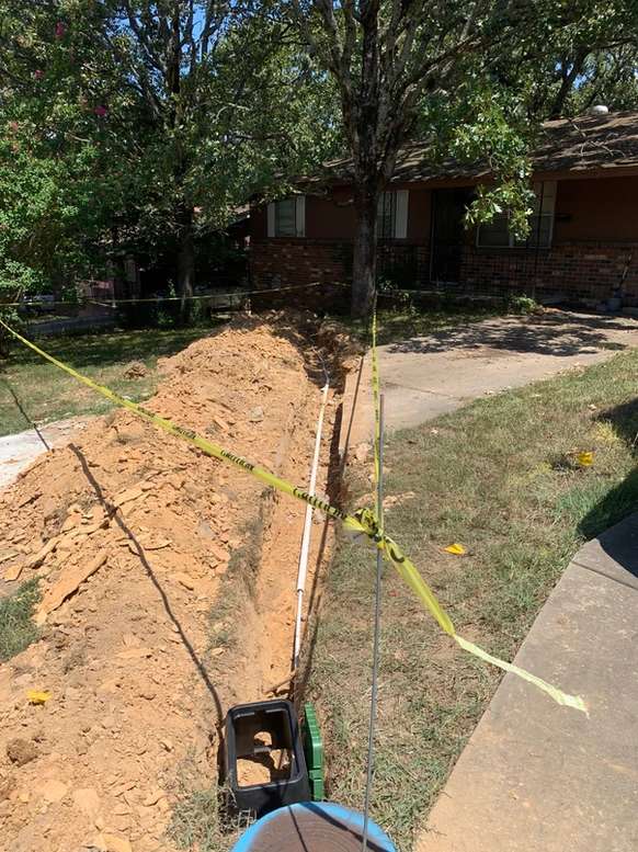 A new water line laying in a narrow ditch in someone's yard. The area has caution tape around it.