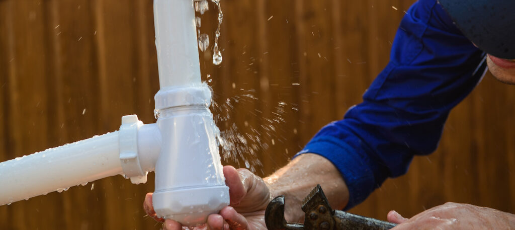 A closeup of hands with a wrench that are fixing a leak in a white pipe.