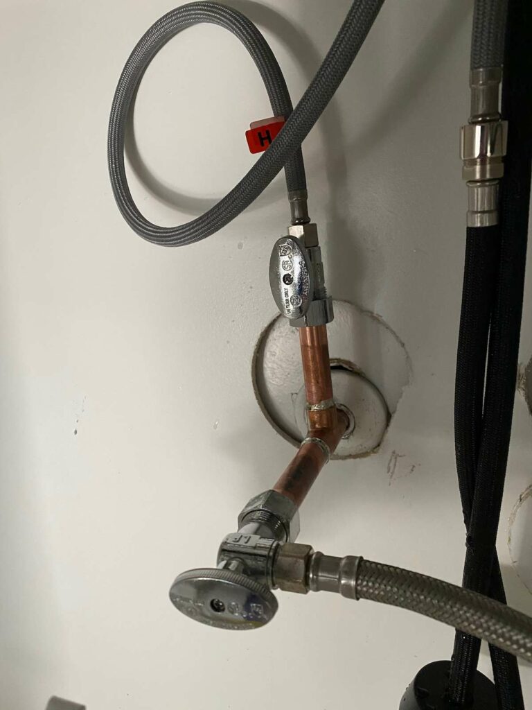 A brand new angle stop valve connected to a gray hose and copper piping coming from a white wall.