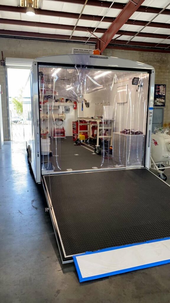 A brand new plumbing liner trailer with the back door open. The doorway is covered in shiny plastic sheets and inside are worktables and tools.