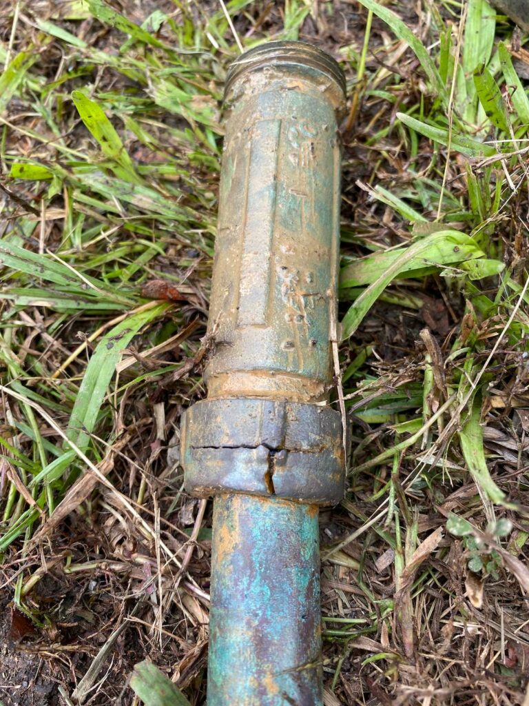 The end of a piece of copper piping that is turning blueish green. A ring around the end of the pipe is cracked in a "T" shape.