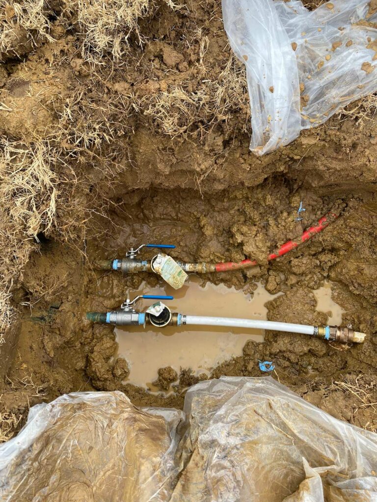 A muddy hole with two pipes sitting at the bottom. Water regulators are attached to both.