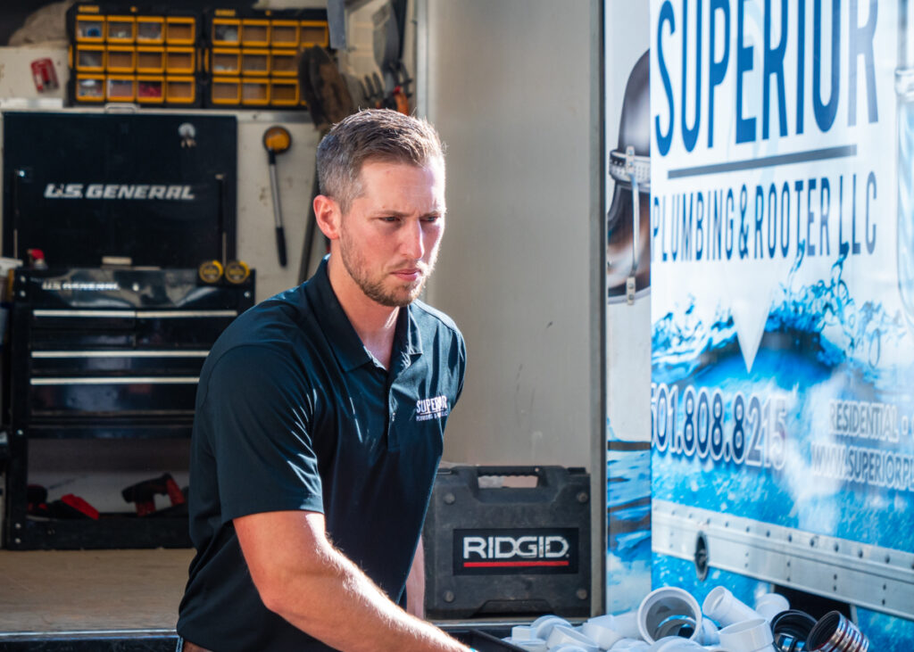 A Superior Plumbing & Rooter LLC employee pushing a black cart full of small pieces of white pipe connectors in front of the company wrapped trailer.