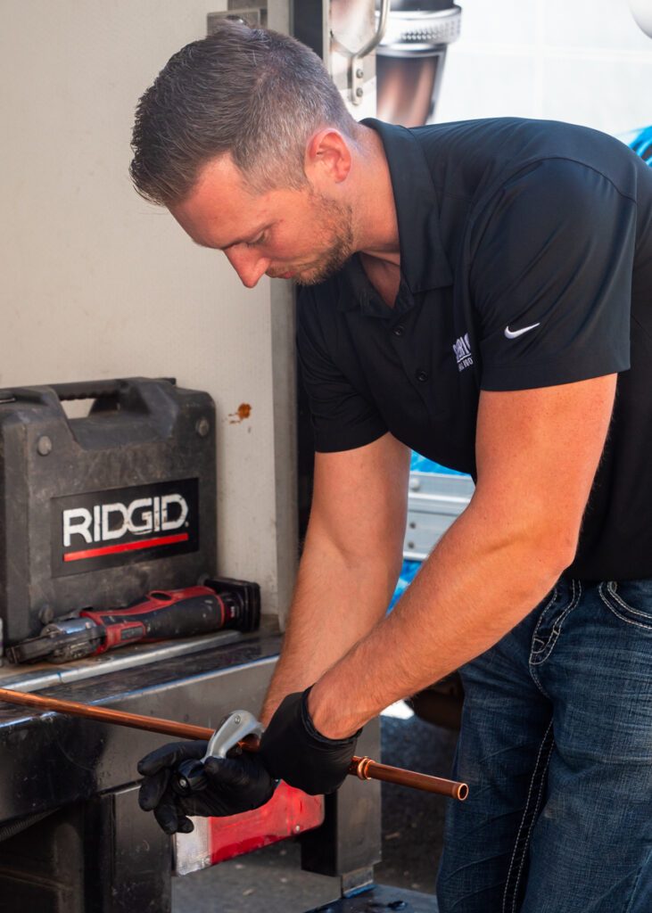 A Superior Plumbing & Rooter employee twists a small silver clamp around a narrow copper pipe.