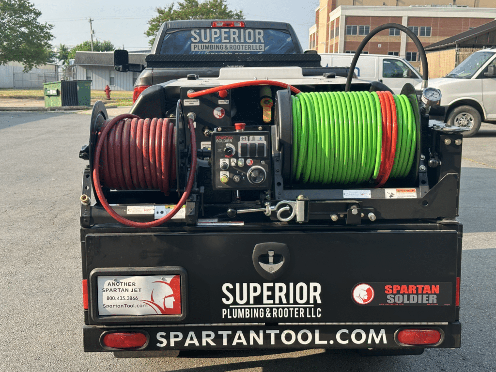 A Superior Plumbing & Rooter LLC truck hauling a trailer of plumbing equipment, including two spools of green pipe and red hose.